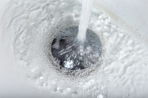 Closeup of tap water flowing into stainless steel drain of white washbasin background in Lithia, FL